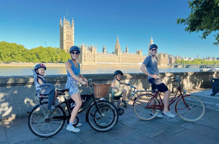 a family posing for a photo with the houses of parliament in the background on a family bike tour of london