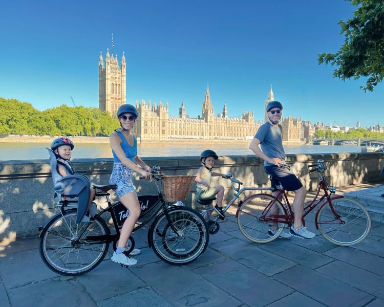 a family posing for a photo with the houses of parliament in the background on a family bike tour of london