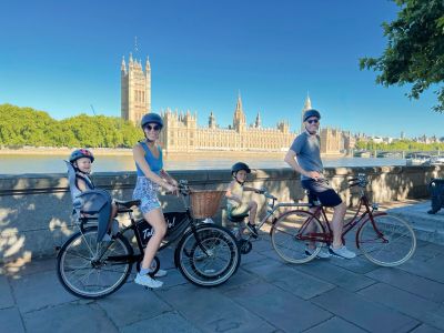a family posing for a photo with the houses of parliament in the background on a family bike tour of london
