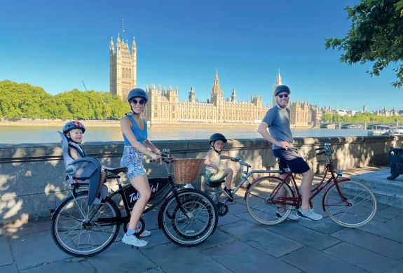 a family posing for a photo with the houses of parliament in the background on a family bike tour of london