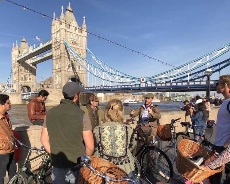 a tour group listening to their guide standing in front of tower bridge on a river thames bike tour