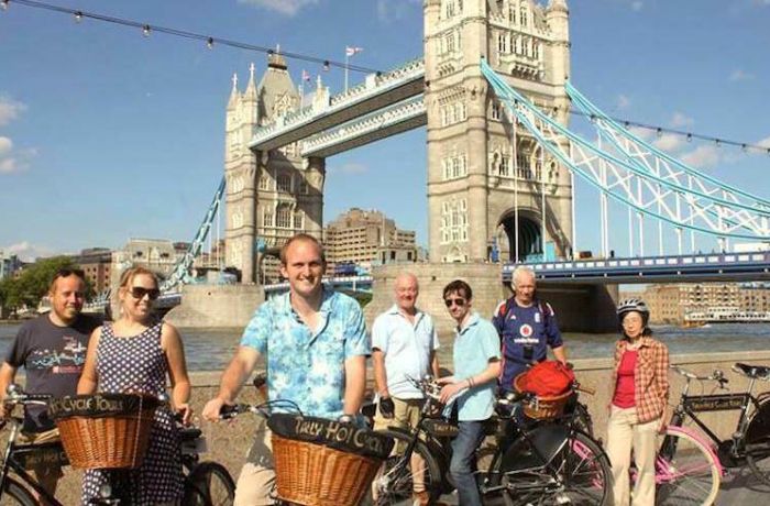 a group of people posing for a photo in front of tower bridge on a river thames bike tour