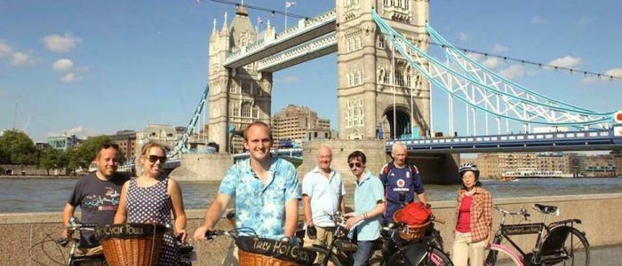 a group of people posing for a photo in front of tower bridge on a river thames bike tour