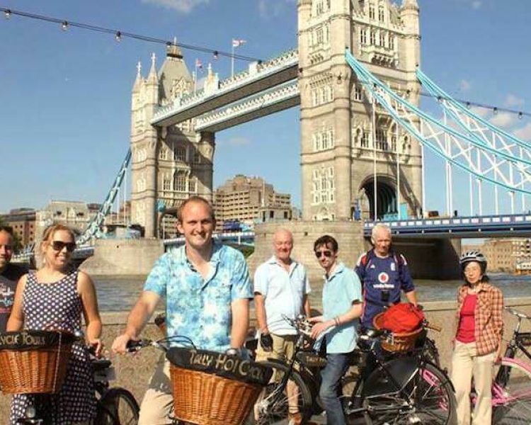 a group of people posing for a photo in front of tower bridge on a river thames bike tour