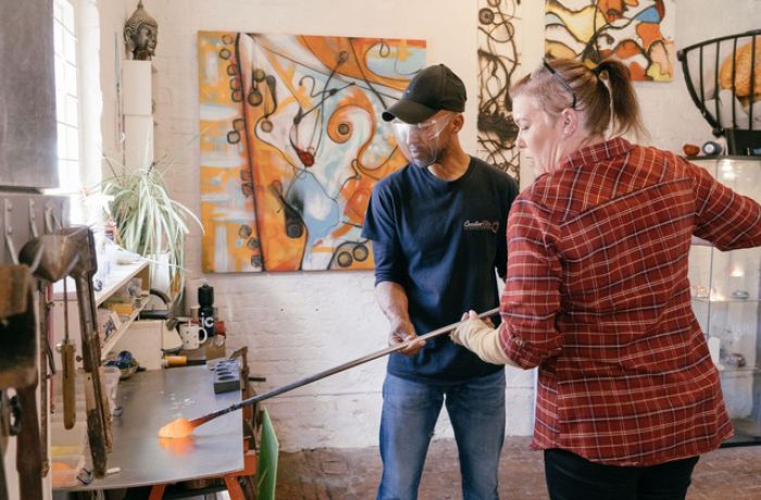 a woman being shown how to do glassblowing in a workshop on a glassblowing experience