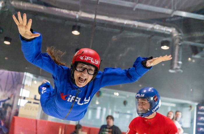 a woman wearing a blue flight suit, goggles and helmet on an indoor skydiving experience