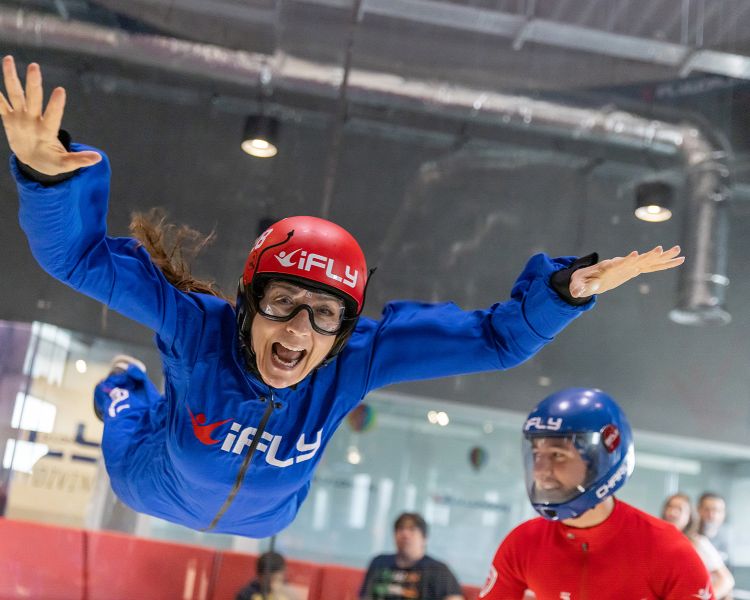 a woman wearing a blue flight suit, goggles and helmet on an indoor skydiving experience