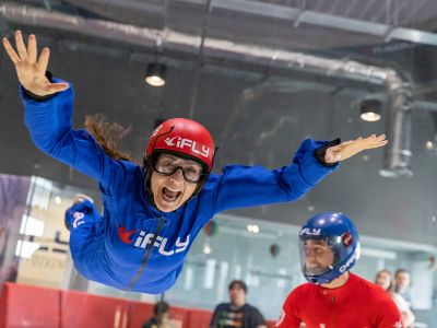 a woman wearing a blue flight suit, goggles and helmet on an indoor skydiving experience