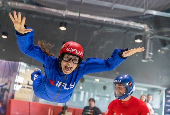 a woman wearing a blue flight suit, goggles and helmet on an indoor skydiving experience