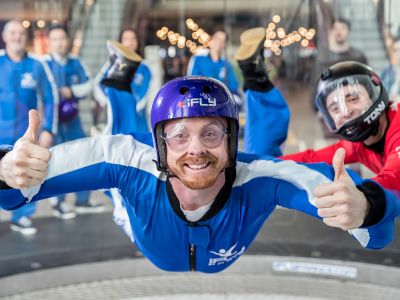 a man wearing a blue flight suit, goggles and helmet giving the thumbs up on an indoor skydiving experience