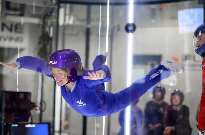 a young girl wearing a blue flight suit, goggles and helmet on an indoor skydiving experience