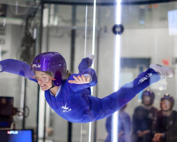 a young girl wearing a blue flight suit, goggles and helmet on an indoor skydiving experience