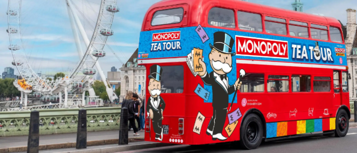 a red routemaster bus with colourful monopoly tea tour signs on it with the london eye in the background