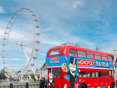 a red routemaster bus with colourful monopoly tea tour signs on it with the london eye in the background