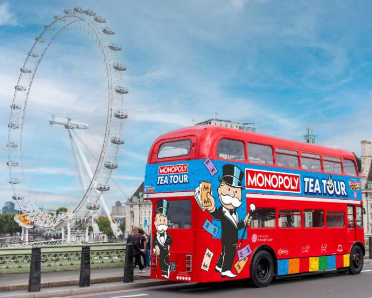 a red routemaster bus with colourful monopoly tea tour signs on it with the london eye in the background