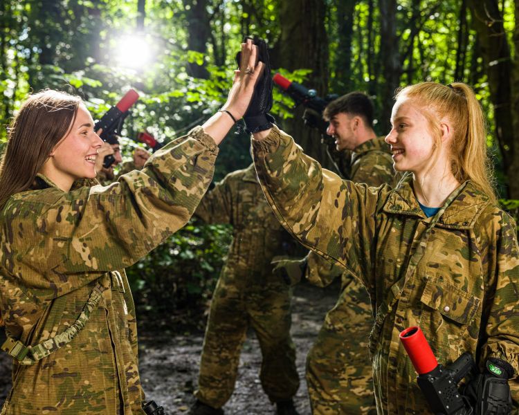 two girls dressed in camouflage gear giving a high five during a game of forest laser tag