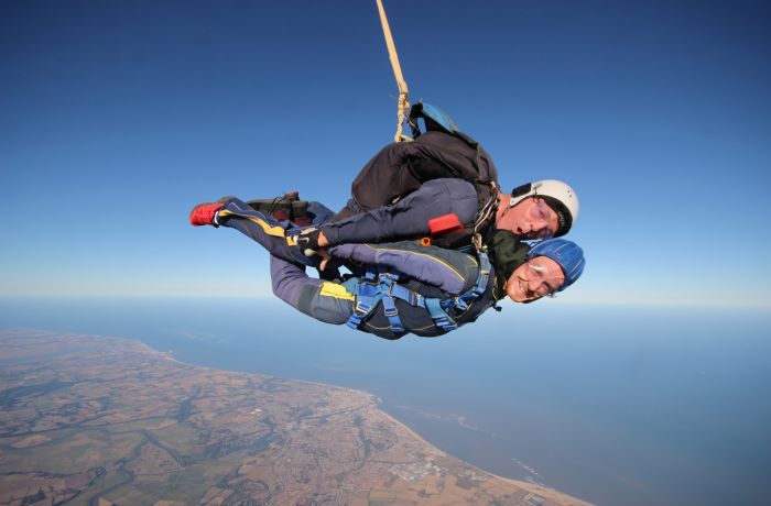 a man on a tandem skydiving experience during freefall with the coastline visible in the distance
