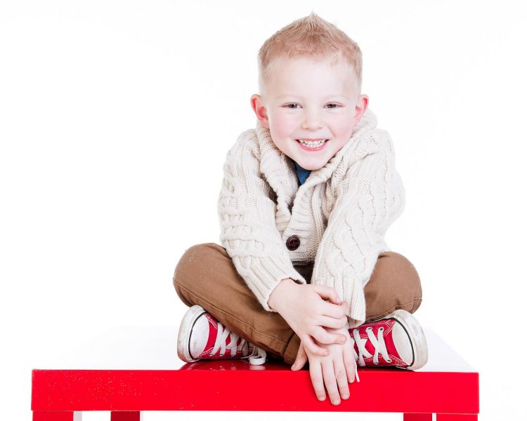 young boy smiling sitting cross legged on a photoshoot