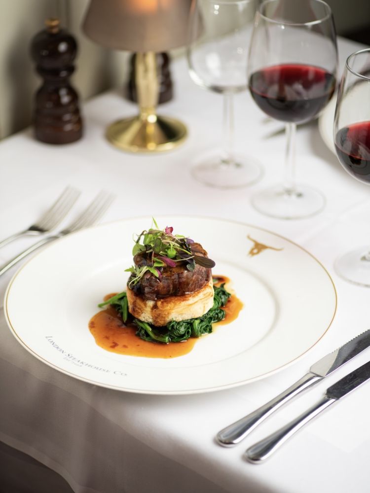 a meal of steak on top of mashed potato and greens at marco pierre white's london steakhouse company