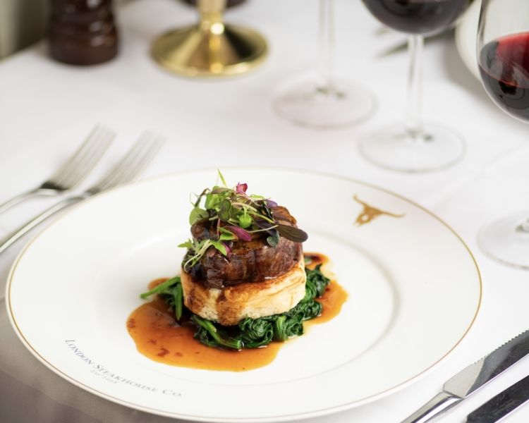 a meal of steak on top of mashed potato and greens at marco pierre white's london steakhouse company