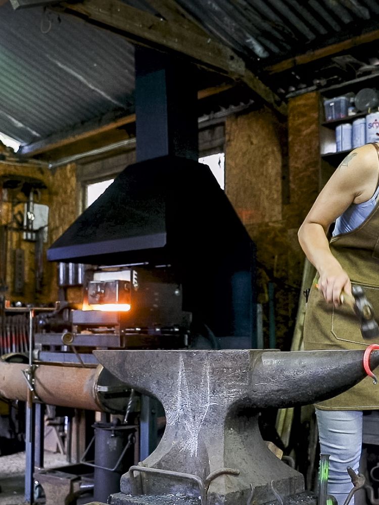 a man and a woman working on a poker at an anvil on a blacksmith experience