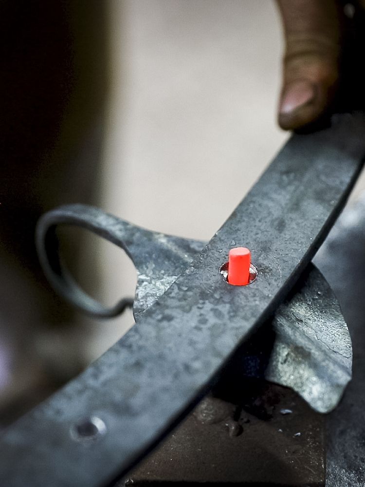 a close up of joining one of the hooks to the rack on a blacksmith experience