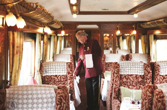 a train steward in traditional smart uniform checking the tables on a vintage style northern belle train carriage