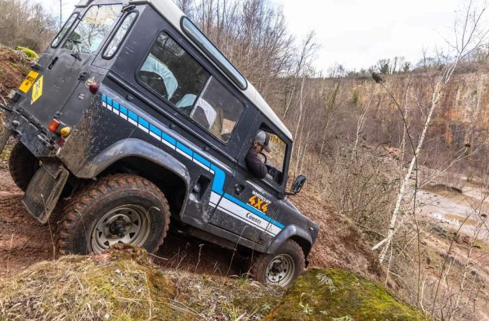 a black land rover off road vehicle driving down a muddy slope on a driving course in gloucestershire