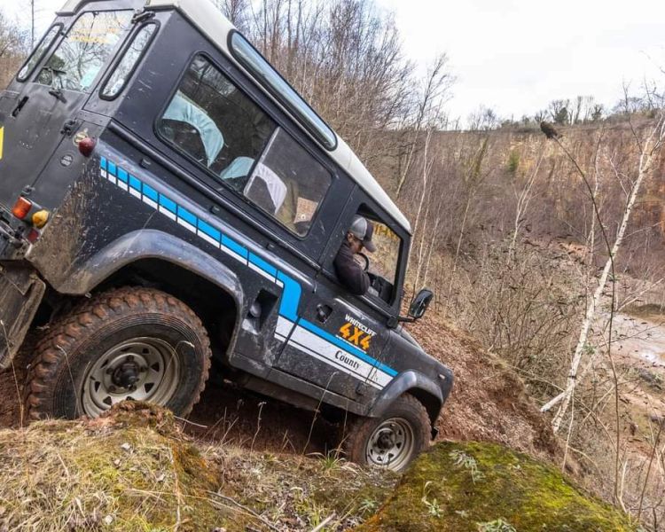 a black land rover off road vehicle driving down a muddy slope on a driving course in gloucestershire