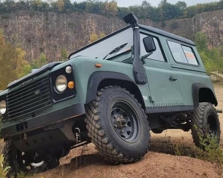 a green land rover off road vehicle driving up a side slope on a driving course in gloucestershire