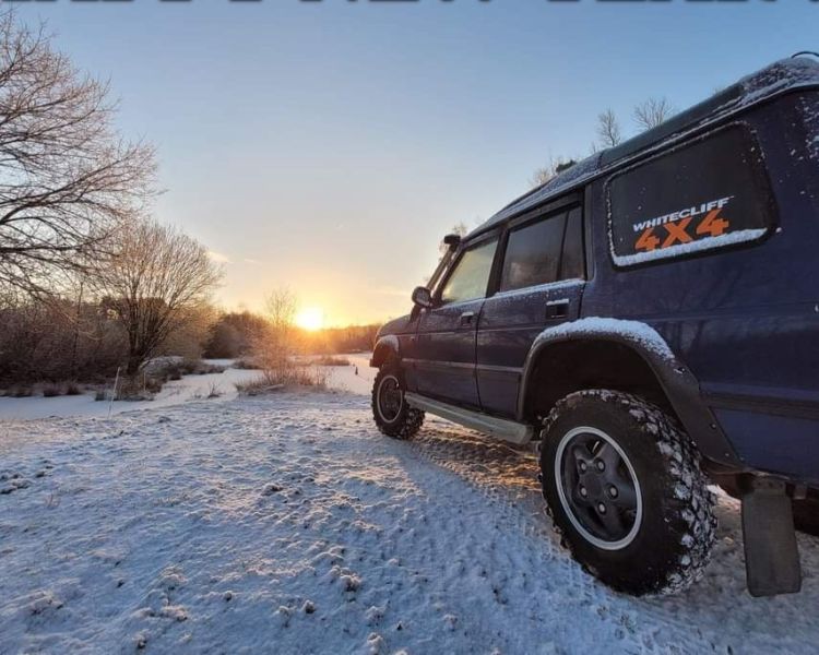 a navy blue land rover off road vehicle on a snowy field on a driving course in gloucestershire