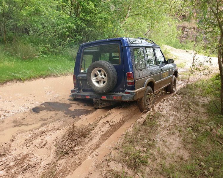 a blue land rover off road vehicle driving along a wet and muddy path on a driving course in gloucestershire