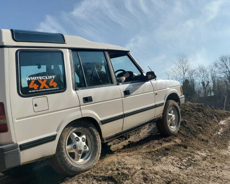 a white land rover off road vehicle driving up a muddy bank on a driving course in gloucestershire