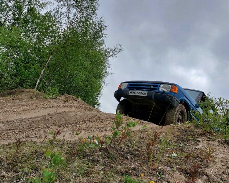 a blue land rover off road vehicle driving up a muddy bank on a driving course in gloucestershire