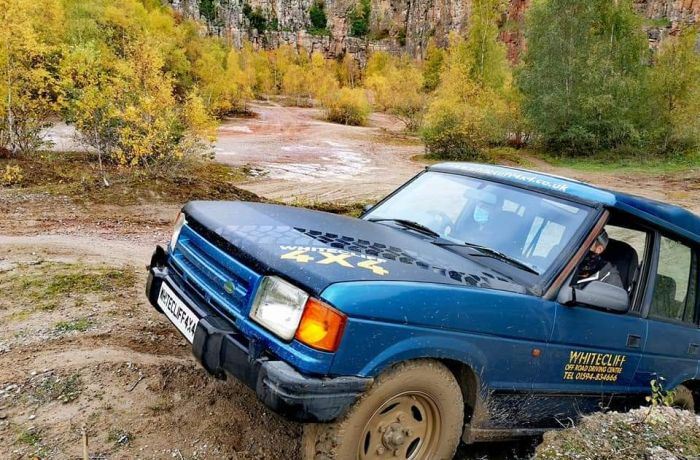a blue land rover off road vehicle driving up a muddy bank on a driving course in gloucestershire