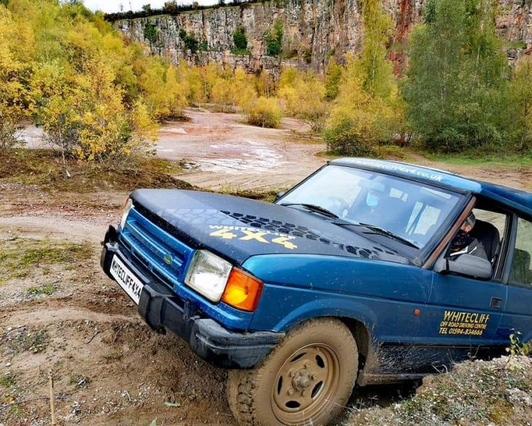 a blue land rover off road vehicle driving up a muddy bank on a driving course in gloucestershire