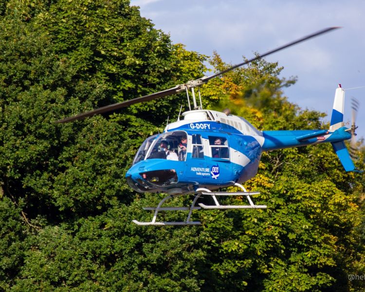 a blue and white helicopter flying amongst trees as part of a 25 mile helicopter trip