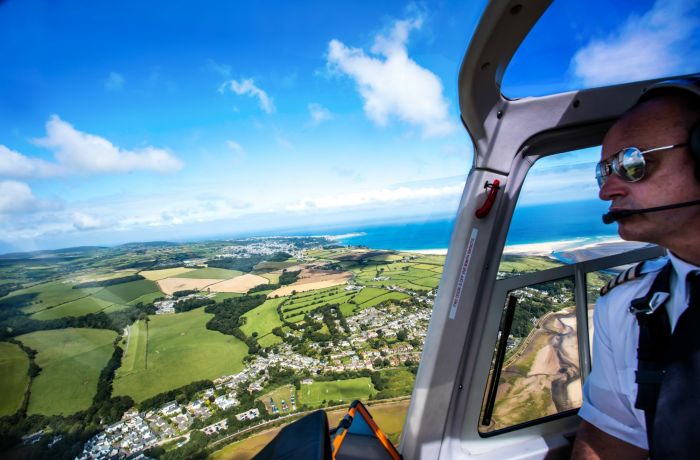 photo taken in the cockpit of a helicopter showing the pilot and the views below of the coastline