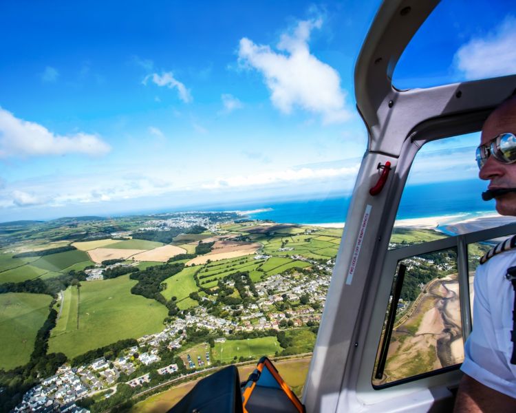 photo taken in the cockpit of a helicopter showing the pilot and the views below of the coastline