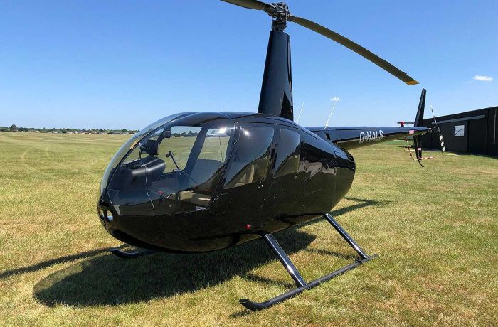 a black helicopter on grass against a blue sky as part of a helicopter flying lesson