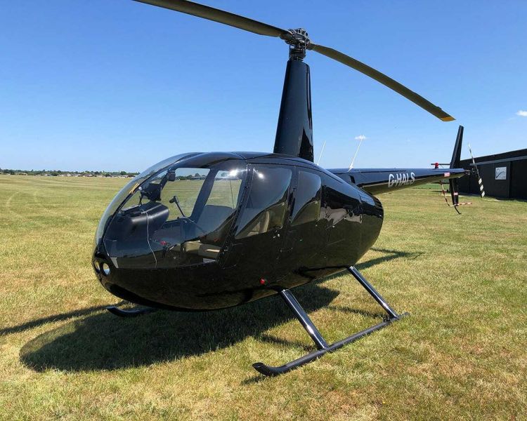 a black helicopter on grass against a blue sky as part of a helicopter flying lesson