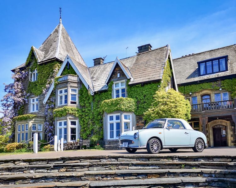 an exterior view of a large country house covered in ivy with a classic car parked out front
