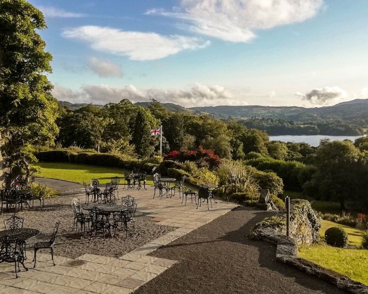 a shot of a terraced area with tables and chairs overlooking trees and a lake in the lake district