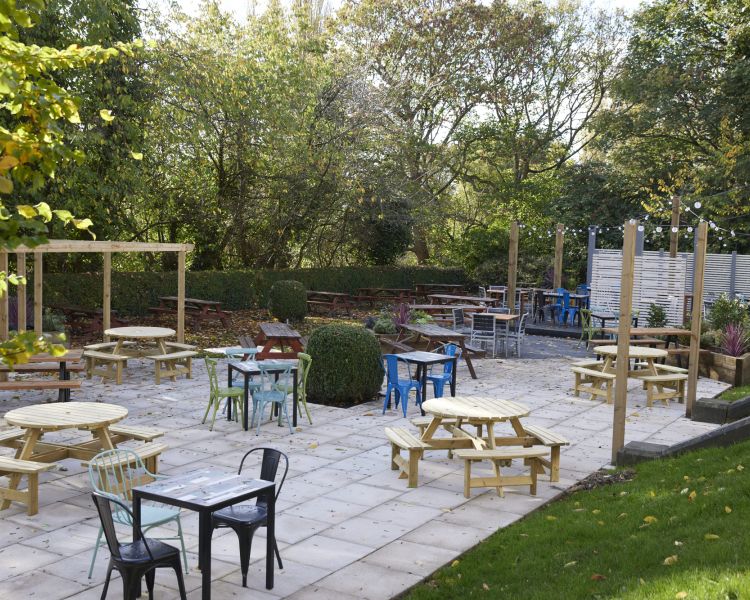 an outside shot of the outdoor seating area at the holmfield arms showing tables and chairs laid out on a patio surrounded by a lawn and trees