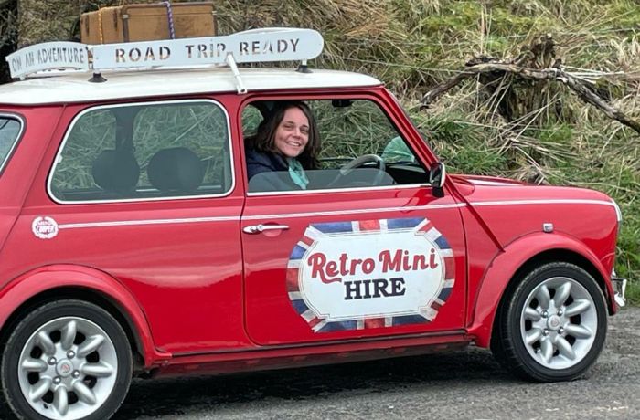 a woman sitting in a classic red mini cooper on a self drive road trip