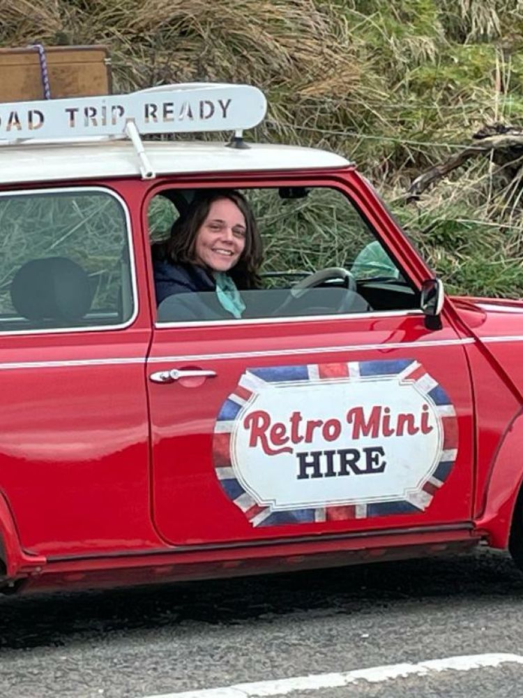 a woman sitting in a classic red mini cooper on a self drive road trip
