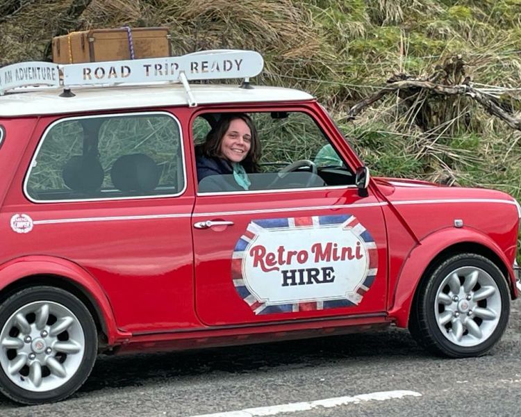 a woman sitting in a classic red mini cooper on a self drive road trip