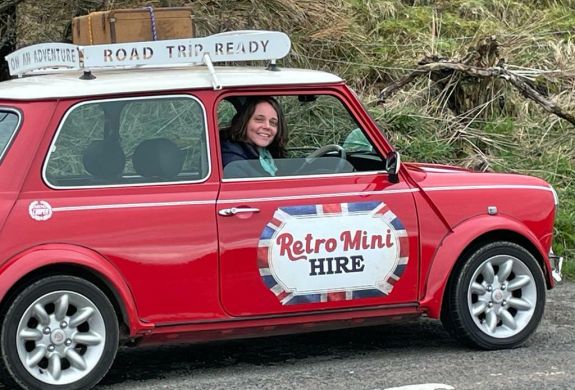 a woman sitting in a classic red mini cooper on a self drive road trip