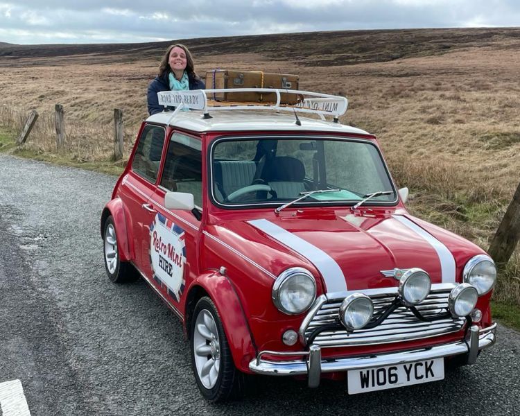 a woman standing behind a classic red mini cooper on a self drive road trip
