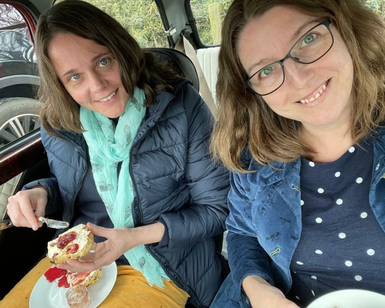 two women eating a cream tea in the back of a classic red mini cooper on a self drive road trip